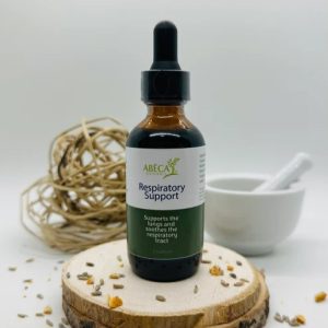 ABĒCA Naturals Respiratory Support tincture bottle on a wooden slice with botanical decorations.