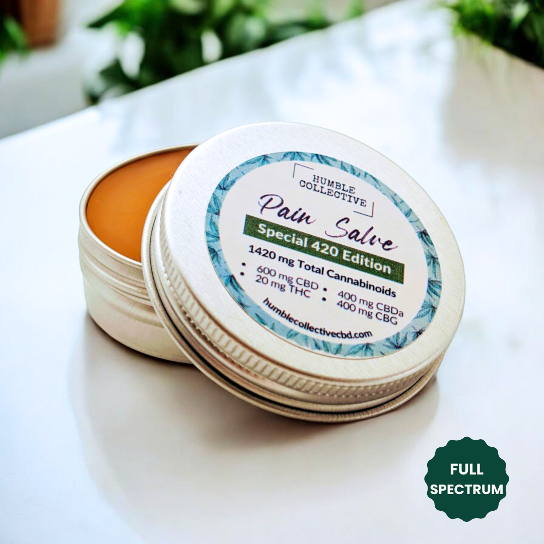 Humble Collective Pain Salve Special 420 Edition – full spectrum herbal salve in a 1 oz tin with 1420 mg total cannabinoids, including 600 mg CBD, 400 mg CBDA, 400 mg CBG, and 20 mg THC, shown open with rich golden balm inside on a white surface with natural lighting.